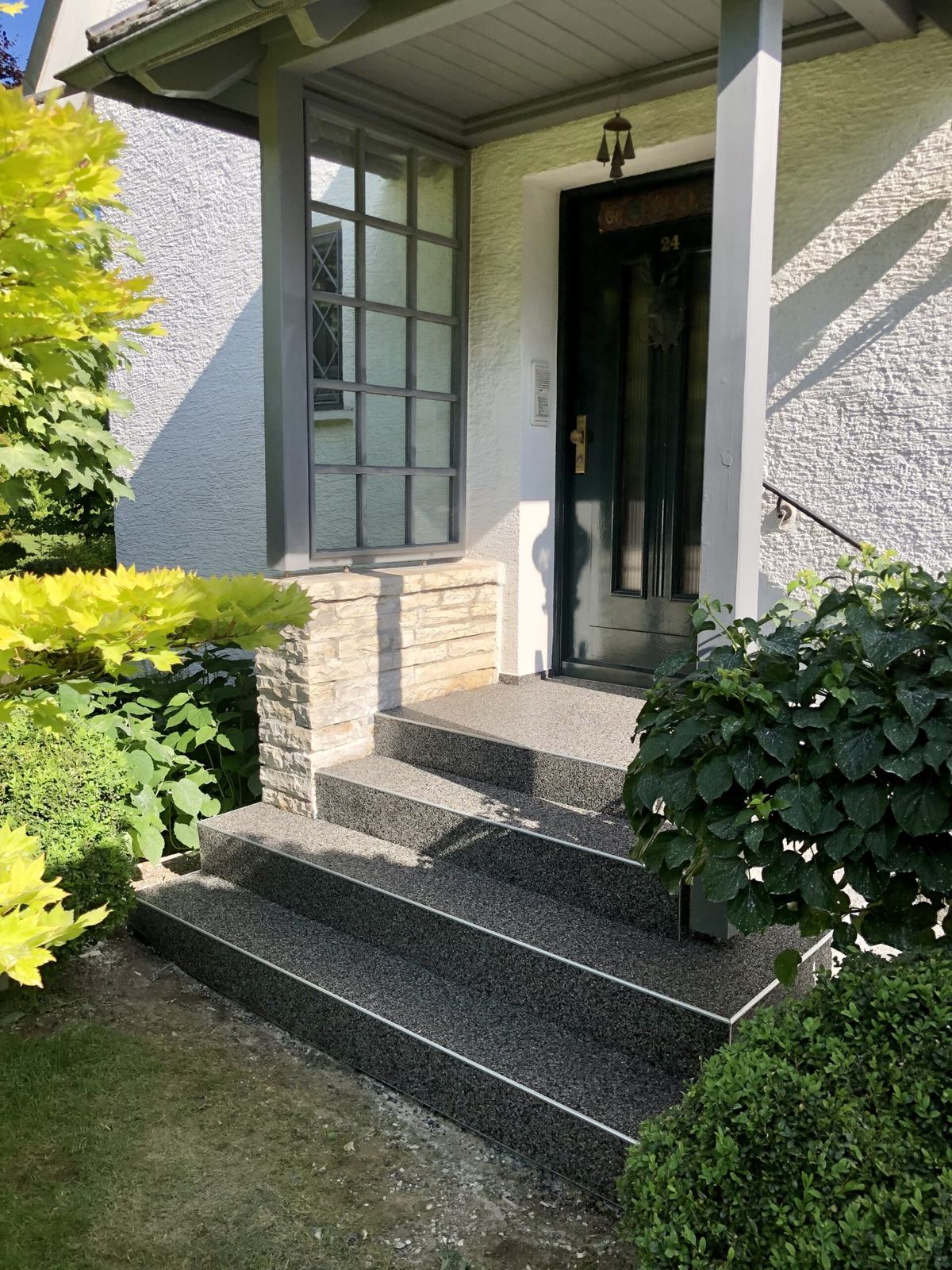 Hauseingang mit anthrazitfarbener Treppe zwischen Buchsbäumen