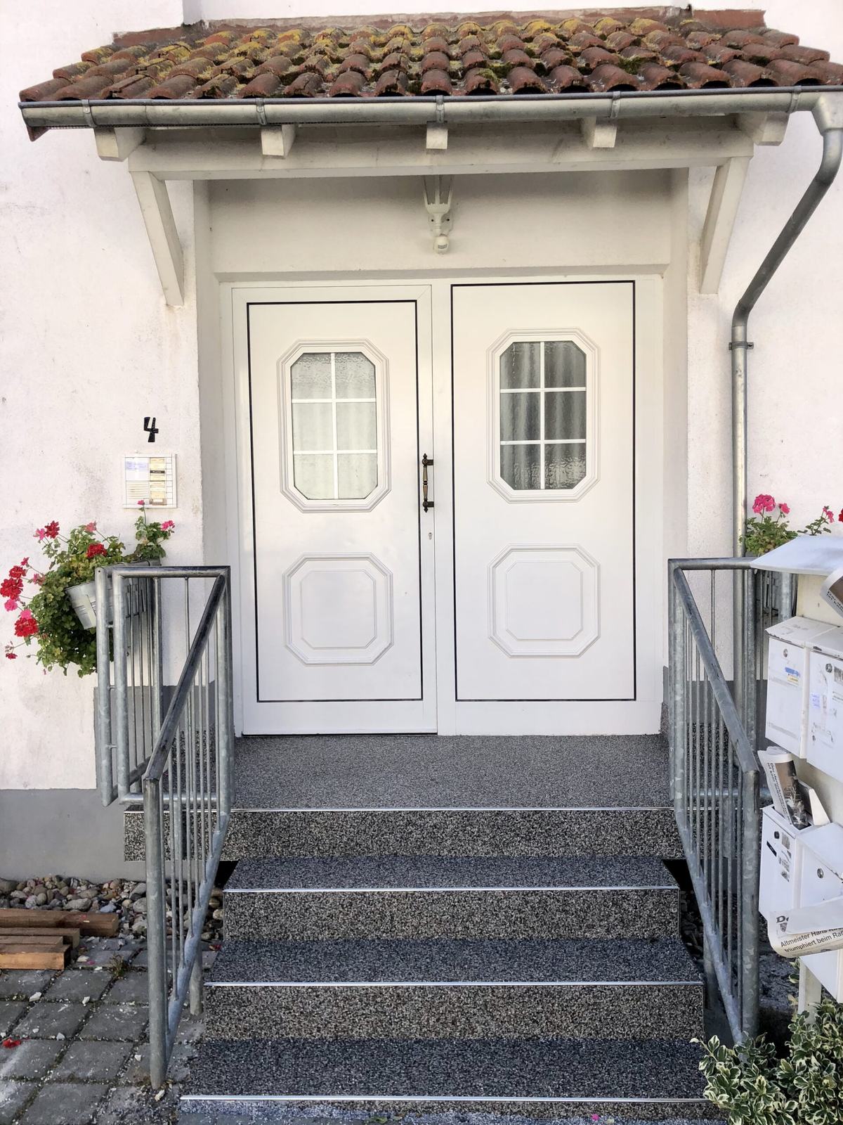 Hauseingang mit weißer Tür und Treppe in grauem Steinteppich