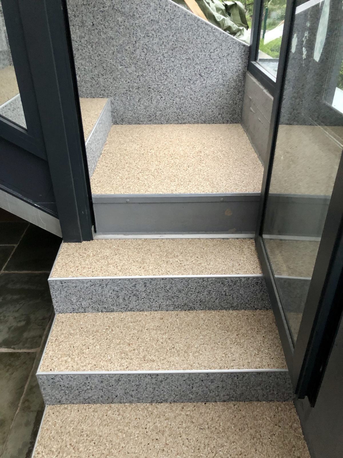 Innentreppe mit hellem Steinteppich und Glasgeländer